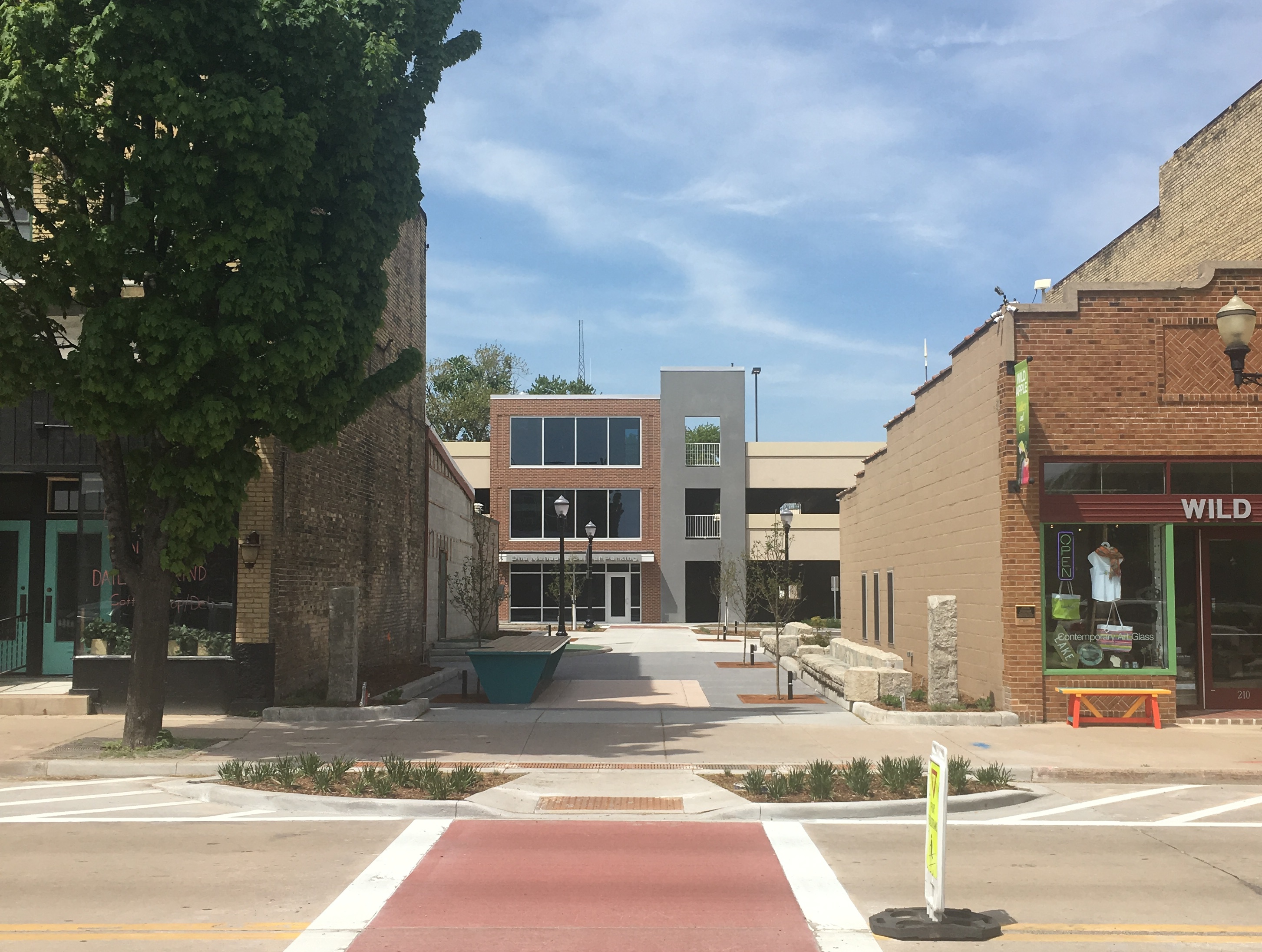 Area of urban renewal (trees, stone benches and several light poles) between two existing buildings in the city of Menasha.